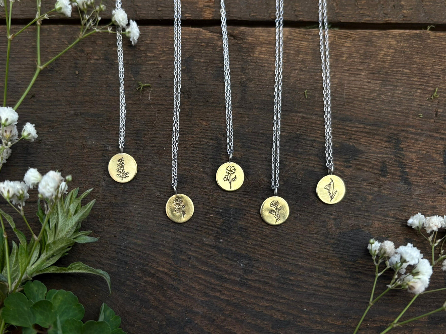 Five necklaces with circular pendants on a wooden surface with birth flowers.