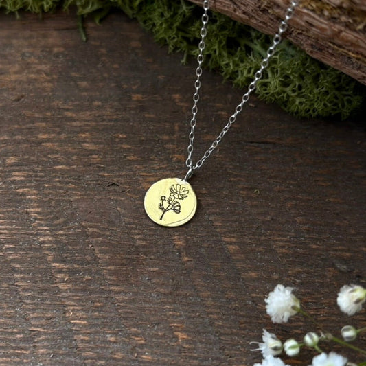 Gold birth flower necklace with a floral pendant on a wooden surface with moss and small flowers. October birth flower, Cosmos