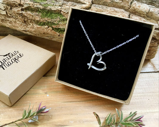 Silver necklace with a heart pendant in a black box on a wooden surface.